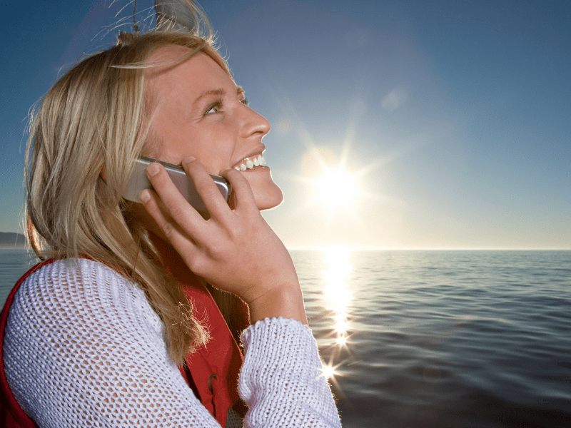 Woman smiling on phone with ocean behind her