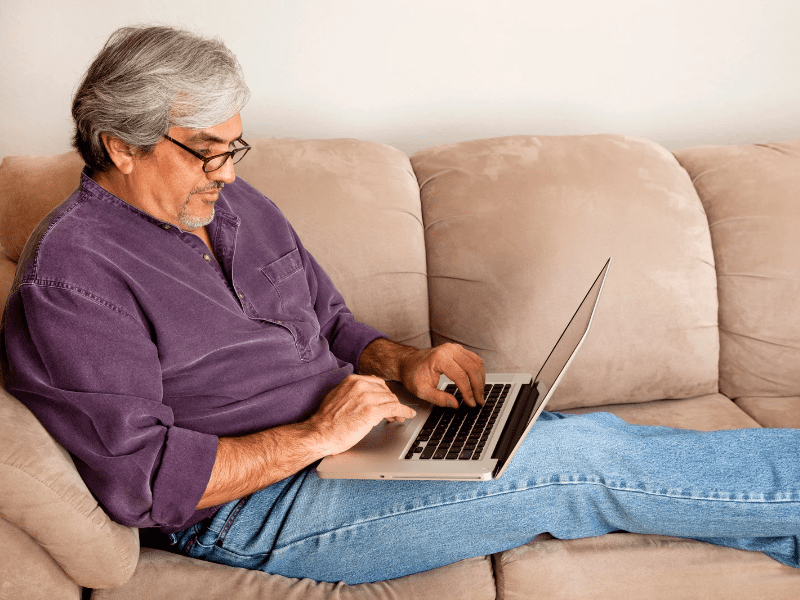 man on sofa while checking his laptop for news