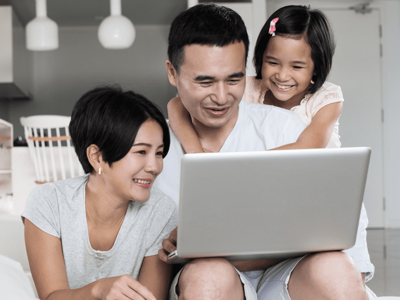 Mother, Father and daughter smiling and looking at one laptop