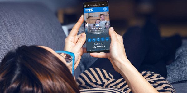 Woman lounges on a couch and views the HTC account login screen on her smartphone.