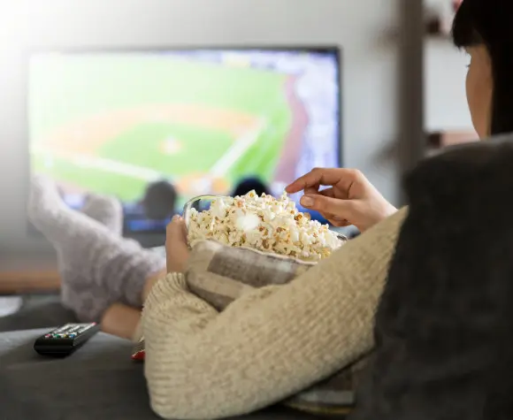 woman eating popcorn, feet up, watching baseball game on tv