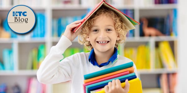 boy in library with a stack of books in hand and one over his head