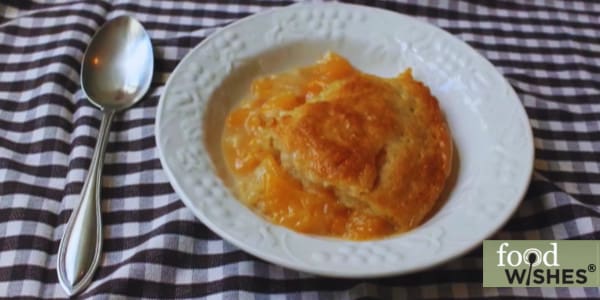 bowl of peach cobbler and spoon on checked tablecloth