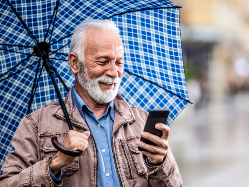 man under plaid umbrella looking at cellphone